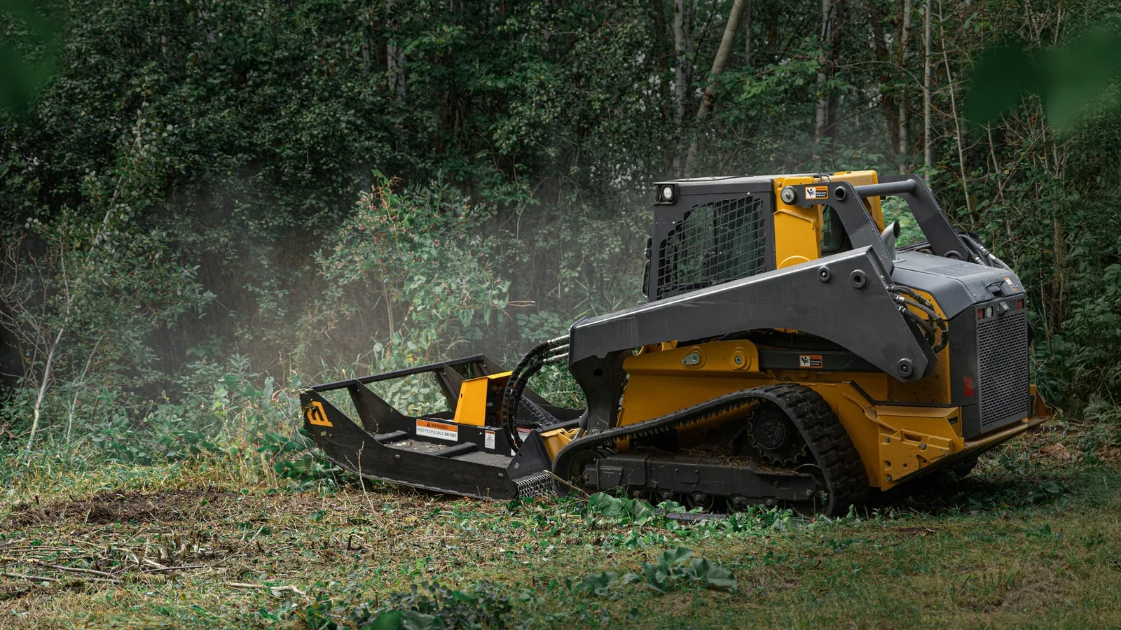 Compact track loader with a brush cutter attachment mowing down heavy green brush