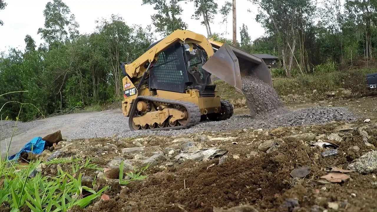 Compact track loader tipping a bucket of gravel out along a new driveway